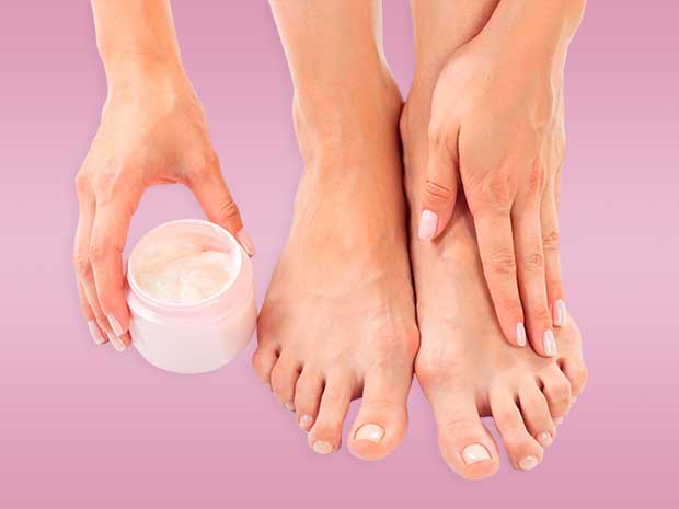 Pés próximos das mãos, com uma das mãos segurando um pote de produto em forma de creme