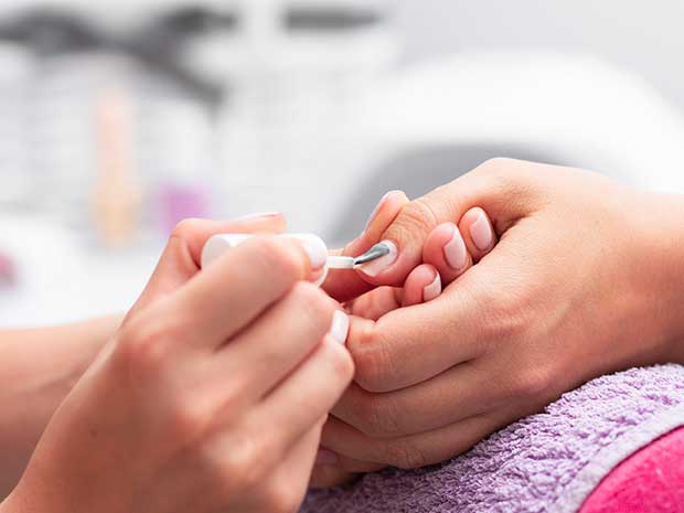 Profissional aplicando um produto nas unhas da cliente.